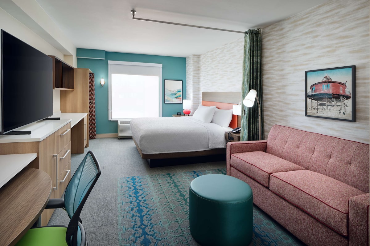 A hotel room with a bed, a sofa, a desk with a TV, and a chair.