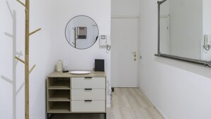 A minimalist bathroom with a wooden coat rack, a round mirror, a white sink, and a small cabinet.