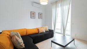 A modern living room with a black sofa, yellow cushions, a small table, and two framed artworks on the wall.