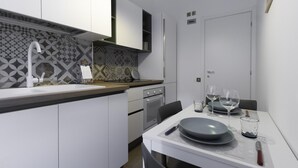 A compact kitchen with a modern design, featuring a white countertop, a built-in oven, and a dining area with a table set for two.
