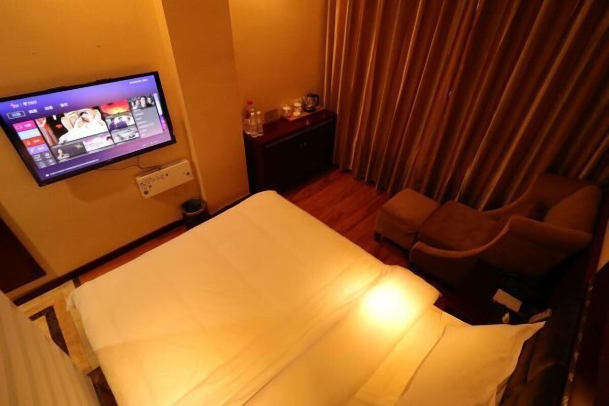 Une chambre d’hôtel avec un lit, un téléviseur fixé au mur, un bureau avec une lampe et une chaise.