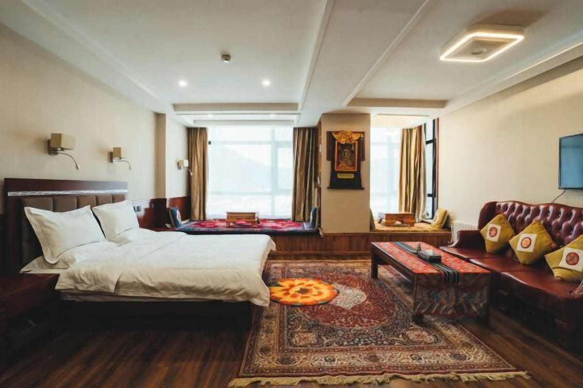 Una habitación de hotel con cama, sofá, mesa de centro y un amplio ventanal con cortinas.