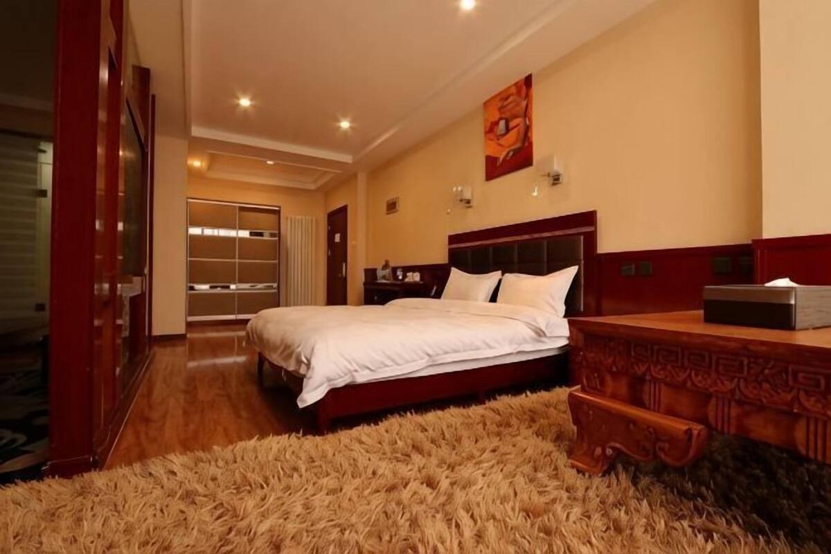 Un dormitorio con una cama, una mesita de noche de madera, un espejo y un ventanal grande.