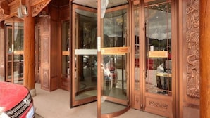A wooden building with a revolving door and glass doors, featuring intricate carvings and a sign above the door. - Norbu Serwo Hotel (Xiahe)