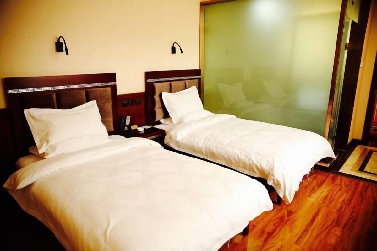 Habitación de hotel con dos camas individuales, cabeceros de madera, una mesita de noche con lámpara y una puerta corrediza de vidrio.