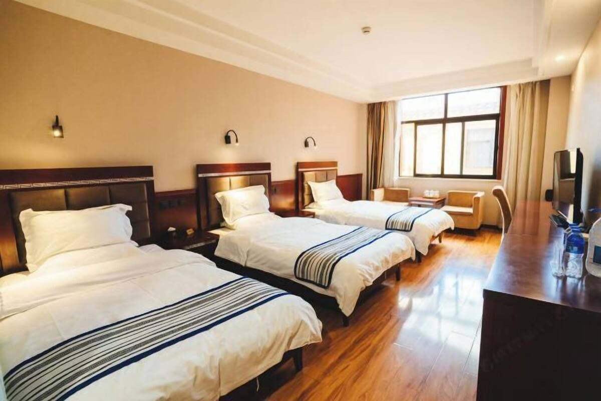 Una habitación de hotel con tres camas, un escritorio, una silla y un televisor.