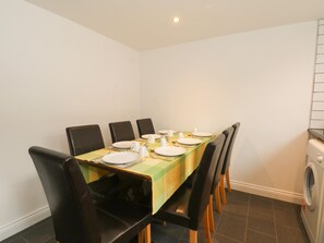 A dining area with a table set for four, surrounded by black chairs, and a washing machine to the right. - Butterfly Cottage (Rossendale)