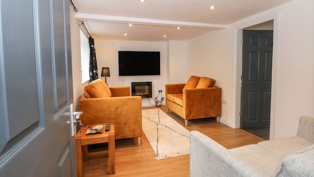 Een moderne woonkamer met een open haard, twee banken, een salontafel en een aan de muur bevestigde televisie.