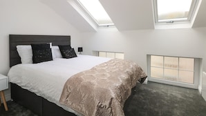 Een slaapkamer met een groot bed, twee dakramen, een nachtkastje en een raam.