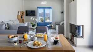 Una sala de estar moderna con una mesa de comedor dispuesta para el desayuno, un sofá y un televisor montado en la pared.