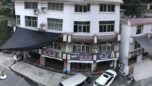 A multi-story building with a flat roof, several ground-level shops, and a parked white car. - Qingyunshan Jieyou Hostel (Yongtai)