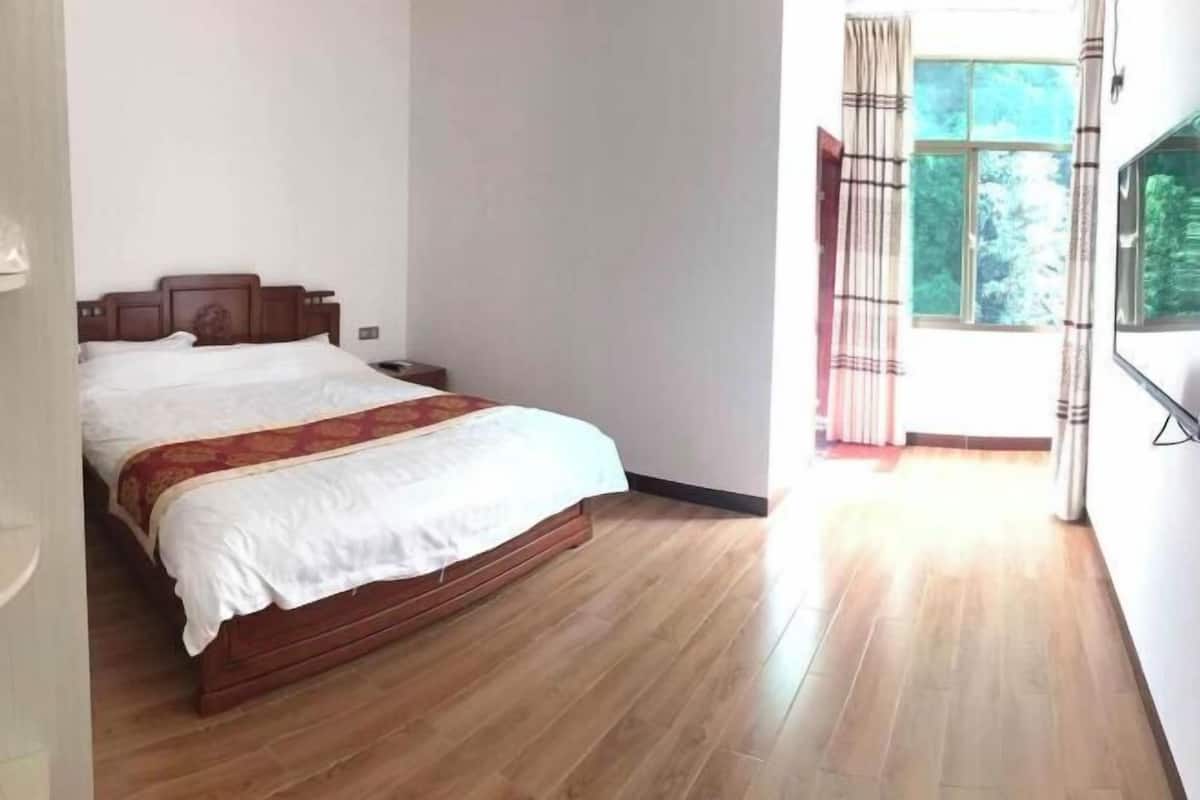 Una camera da letto con un letto di legno, un comodino, una finestra con tende e vista sul verde.