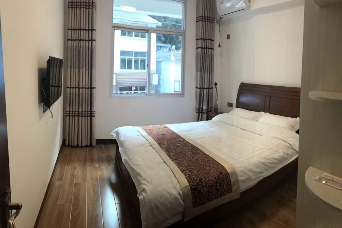 Una camera d'albergo con un letto, una TV a muro, una finestra con tende e una porta.
