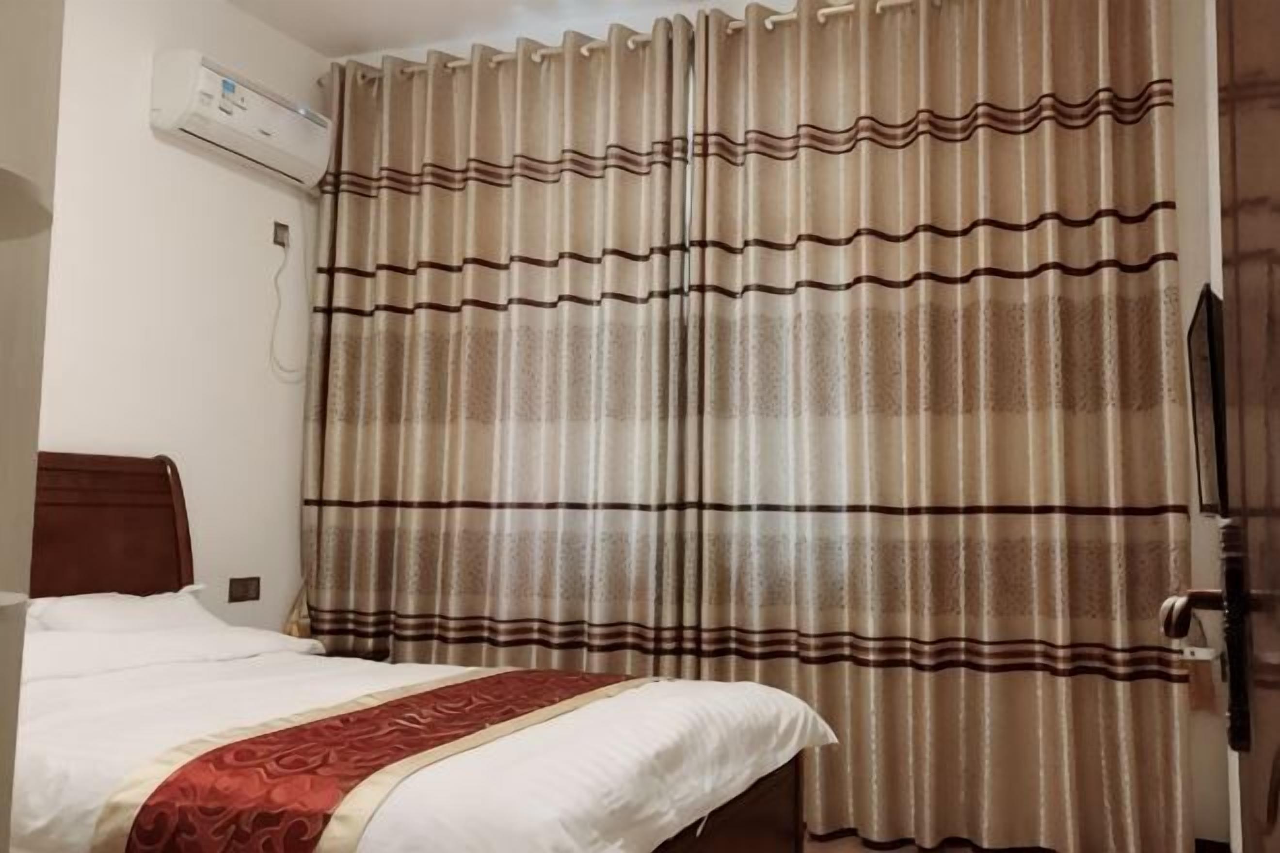 Una habitación de hotel con una cama, cortinas y un equipo de aire acondicionado.