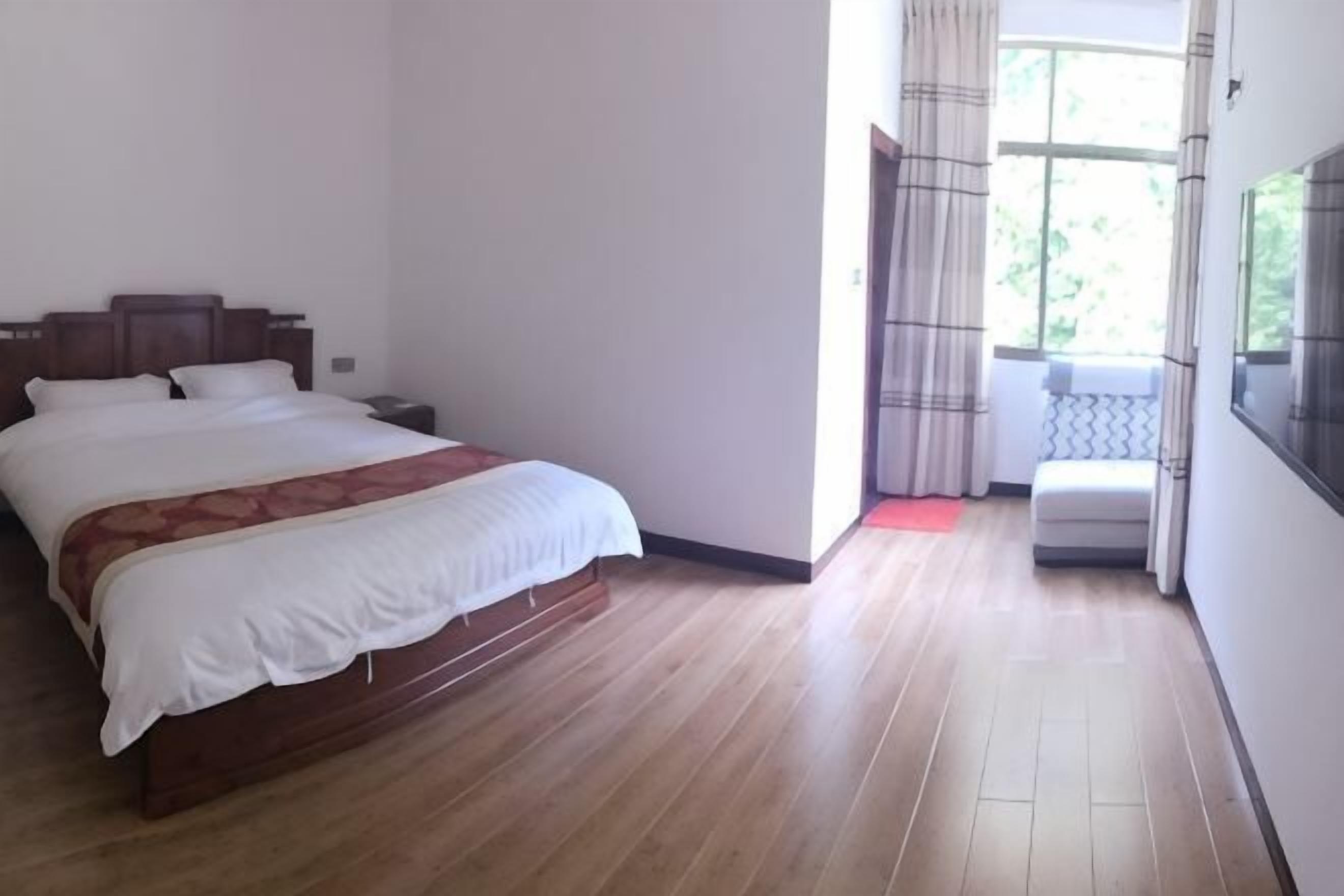 Un dormitorio con cama de madera, mesita de noche, ventana con cortinas y vista a zonas verdes.