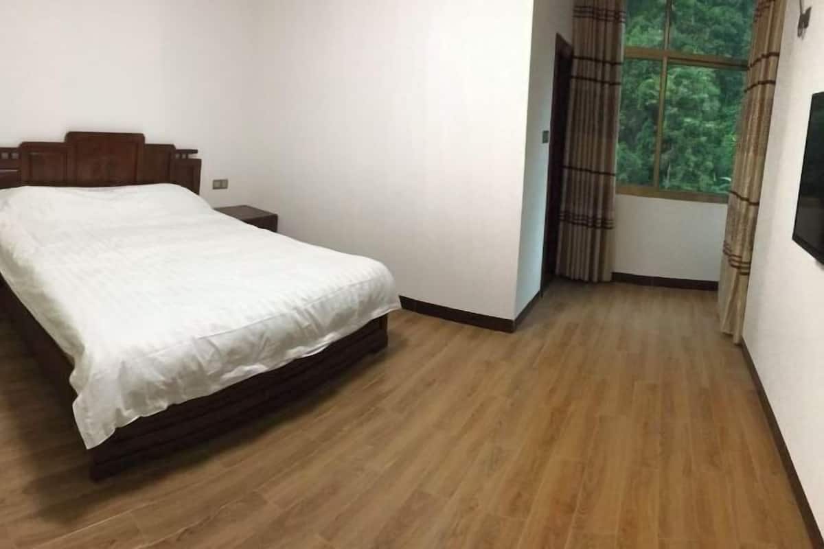 Una camera da letto con un letto, un comodino, una finestra con tende e una TV appesa al muro.