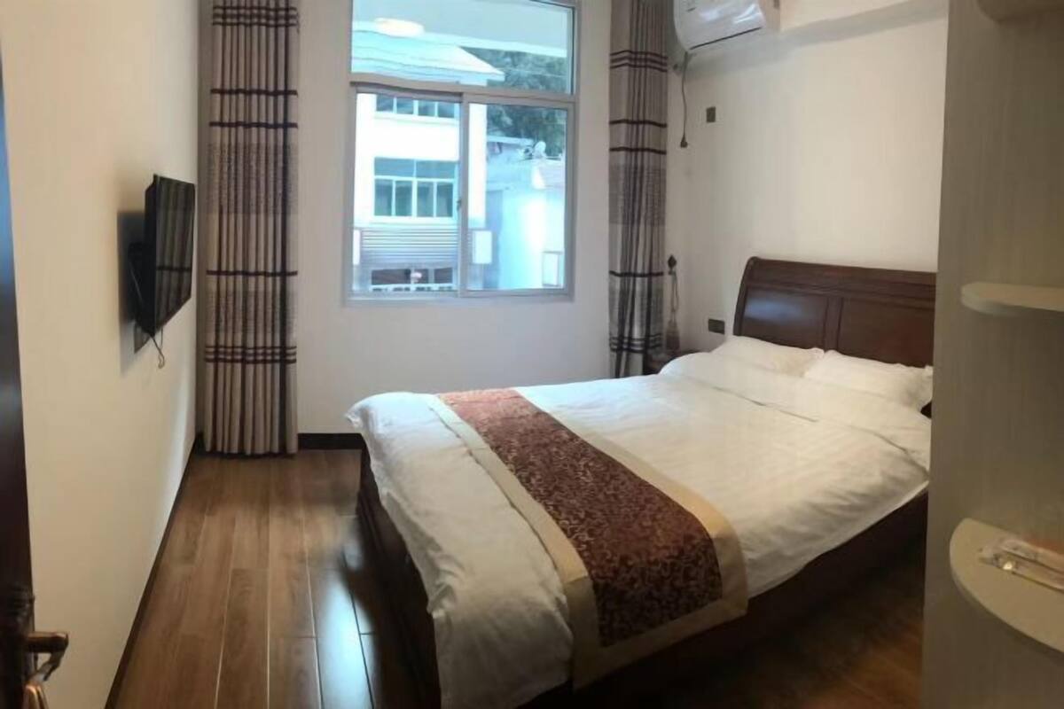 Una camera da letto con un letto, una finestra, tende e una TV a parete.