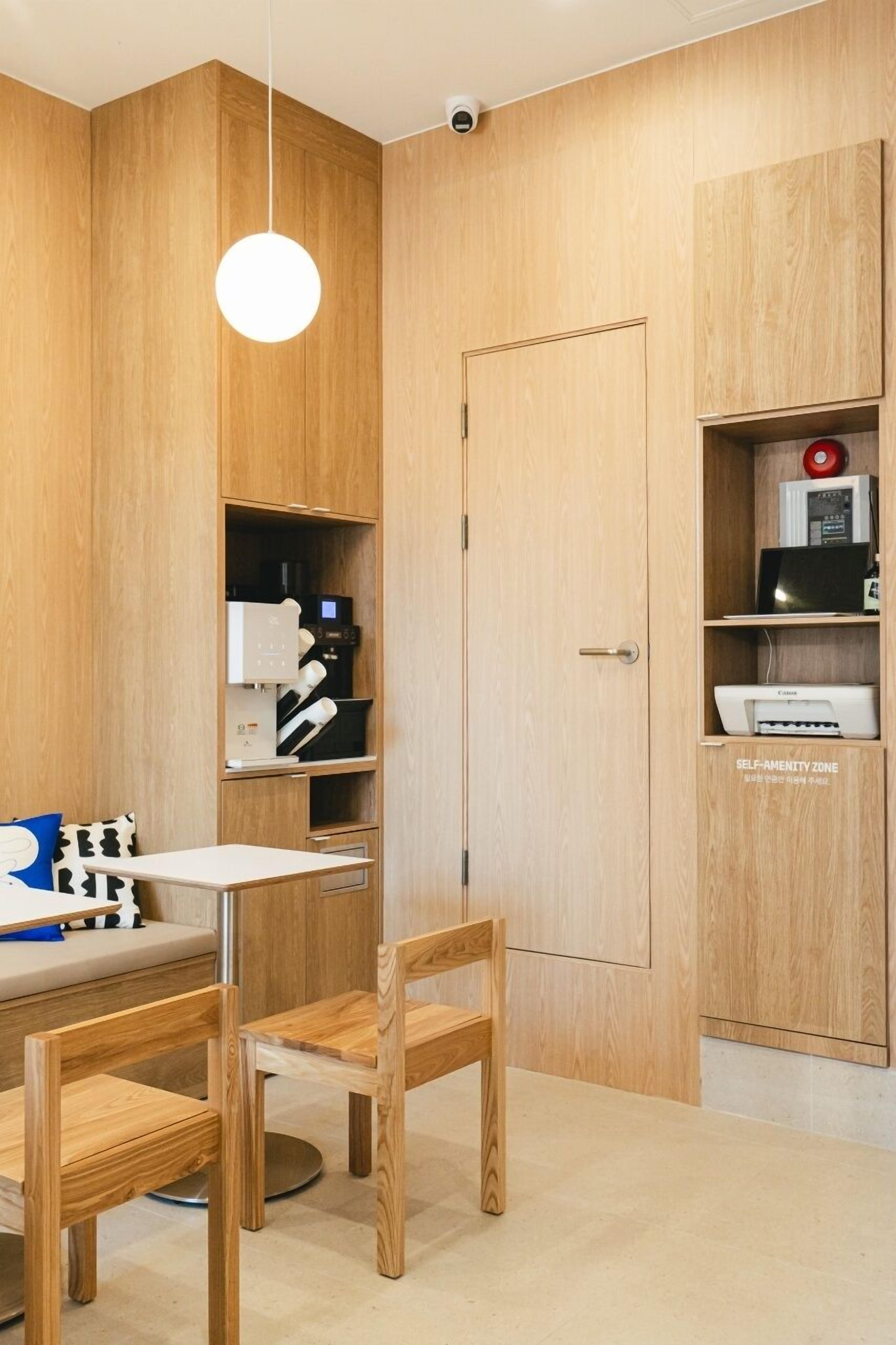 A modern room with wooden panel walls, a round pendant light, a coffee machine, a printer, and a self-service kiosk.