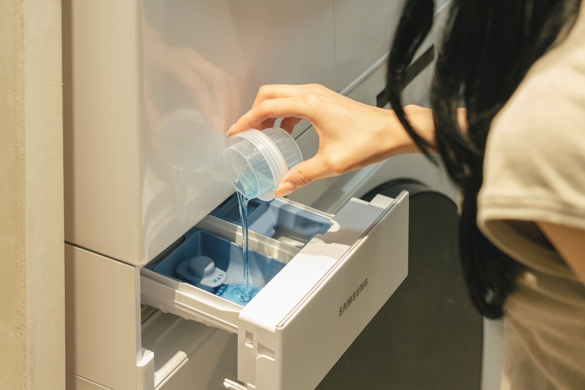 Una persona vertiendo agua desde un recipiente de plástico en un cajón de nevera Samsung.