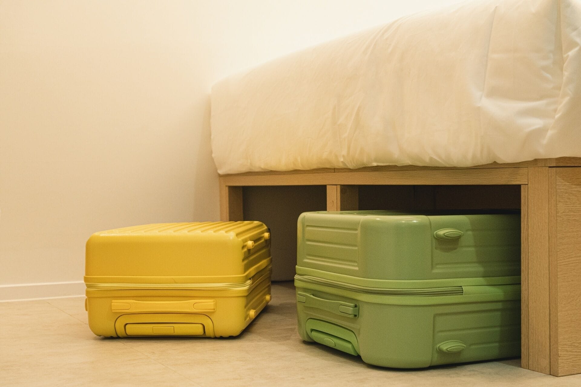 Two suitcases, one yellow and one green, placed under a bed with a white mattress.