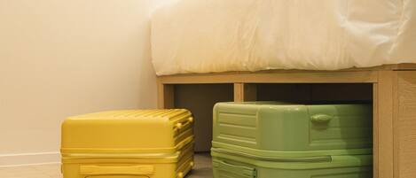 Two suitcases, one yellow and one green, placed under a bed with a white mattress.