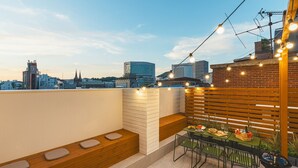Una terraza en la azotea con una mesa para dos, una parrilla y vistas al horizonte de la ciudad.