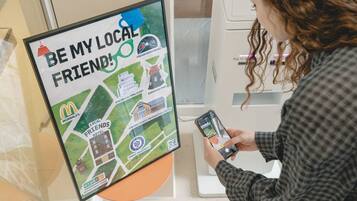 A person using a smartphone to interact with a digital map display titled "BE MY LOCAL FRIENDS".