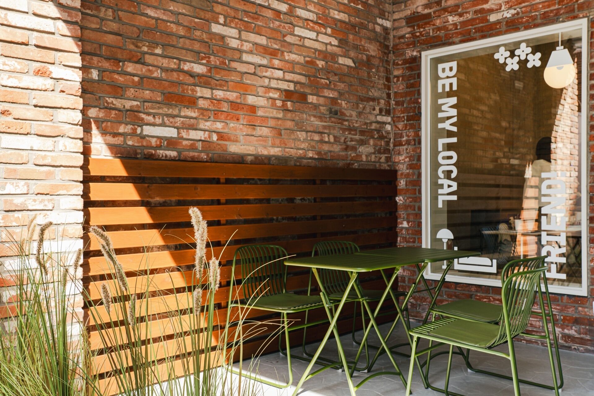An outdoor seating area with a brick wall, wooden slats, and green metal chairs.
