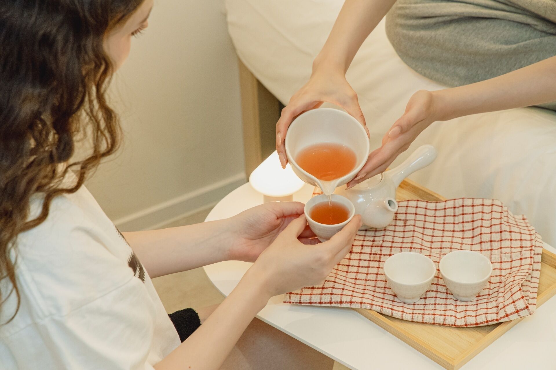 A person pouring tea into a cup on a tray with two other cups.