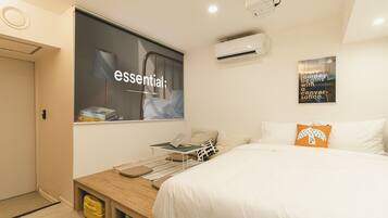 Una habitación de hotel con una cama, un escritorio con una computadora portátil, un aire acondicionado y un cartel en la pared.
