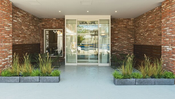 Entrada de un hotel con paredes de ladrillo, puerta de cristal y plantas de interior.