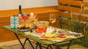 Una mesa servida con comida, bebidas y una botella de vino en una terraza de madera.