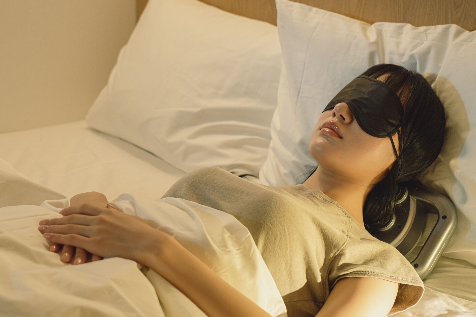 A person lying in a bed with white bedding and a headrest.