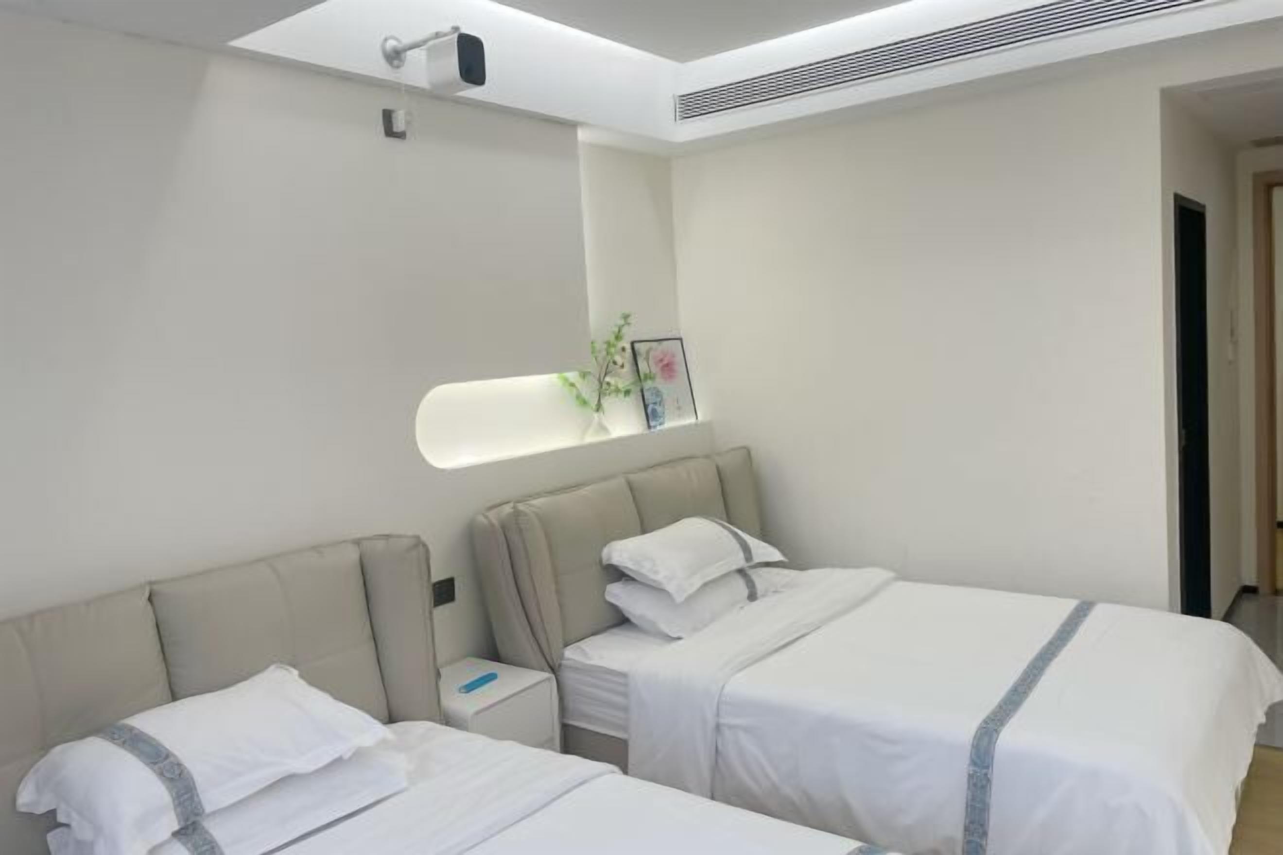 A hotel room with two beds, a nightstand, a mirror, and a small plant.