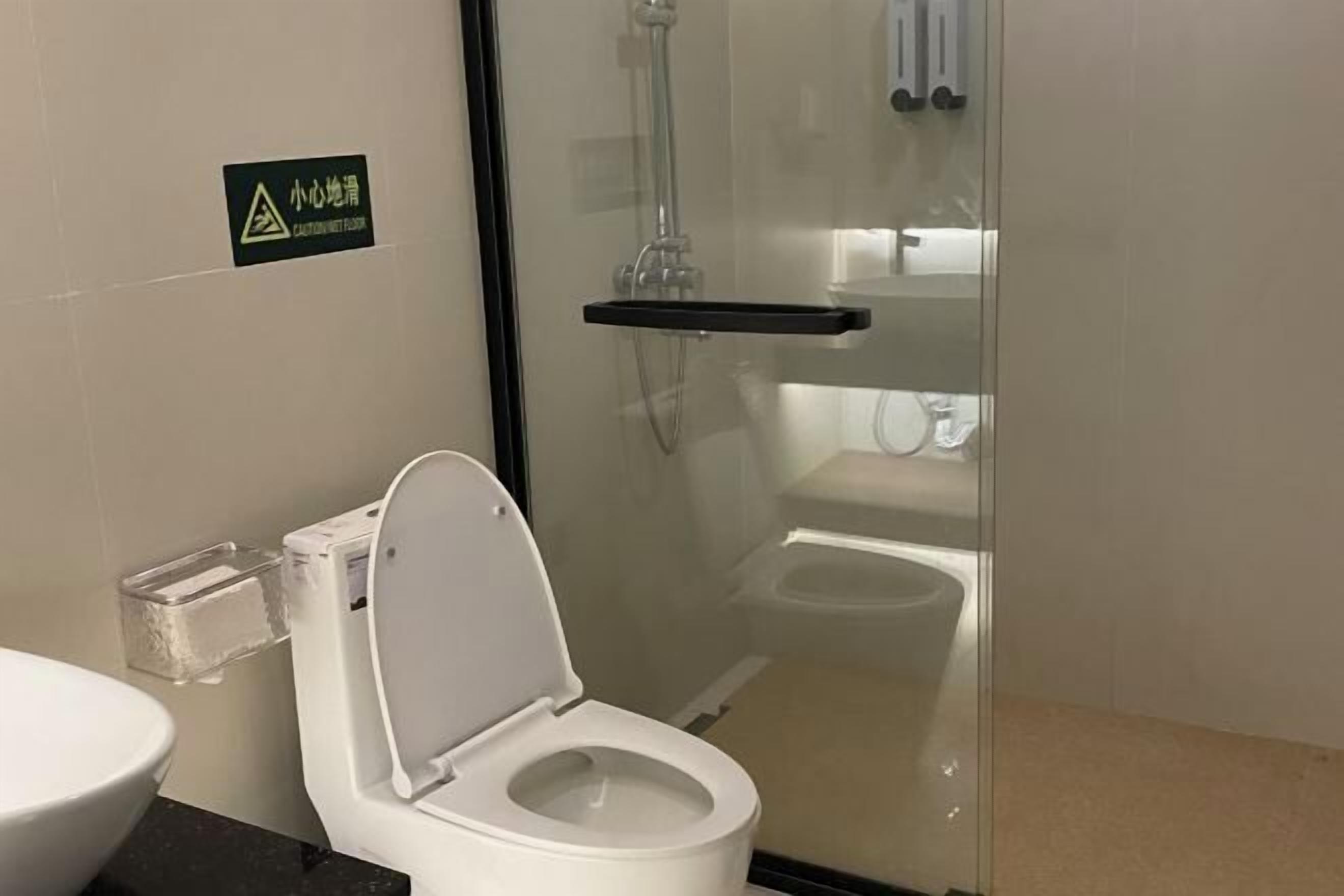 Un baño moderno con ducha de vidrio, inodoro blanco y cubo de plástico transparente.