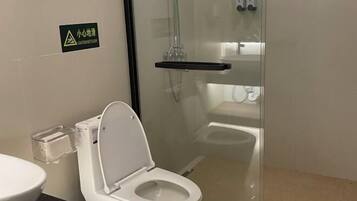 Un baño moderno con ducha de vidrio, inodoro blanco y cubo de plástico transparente.