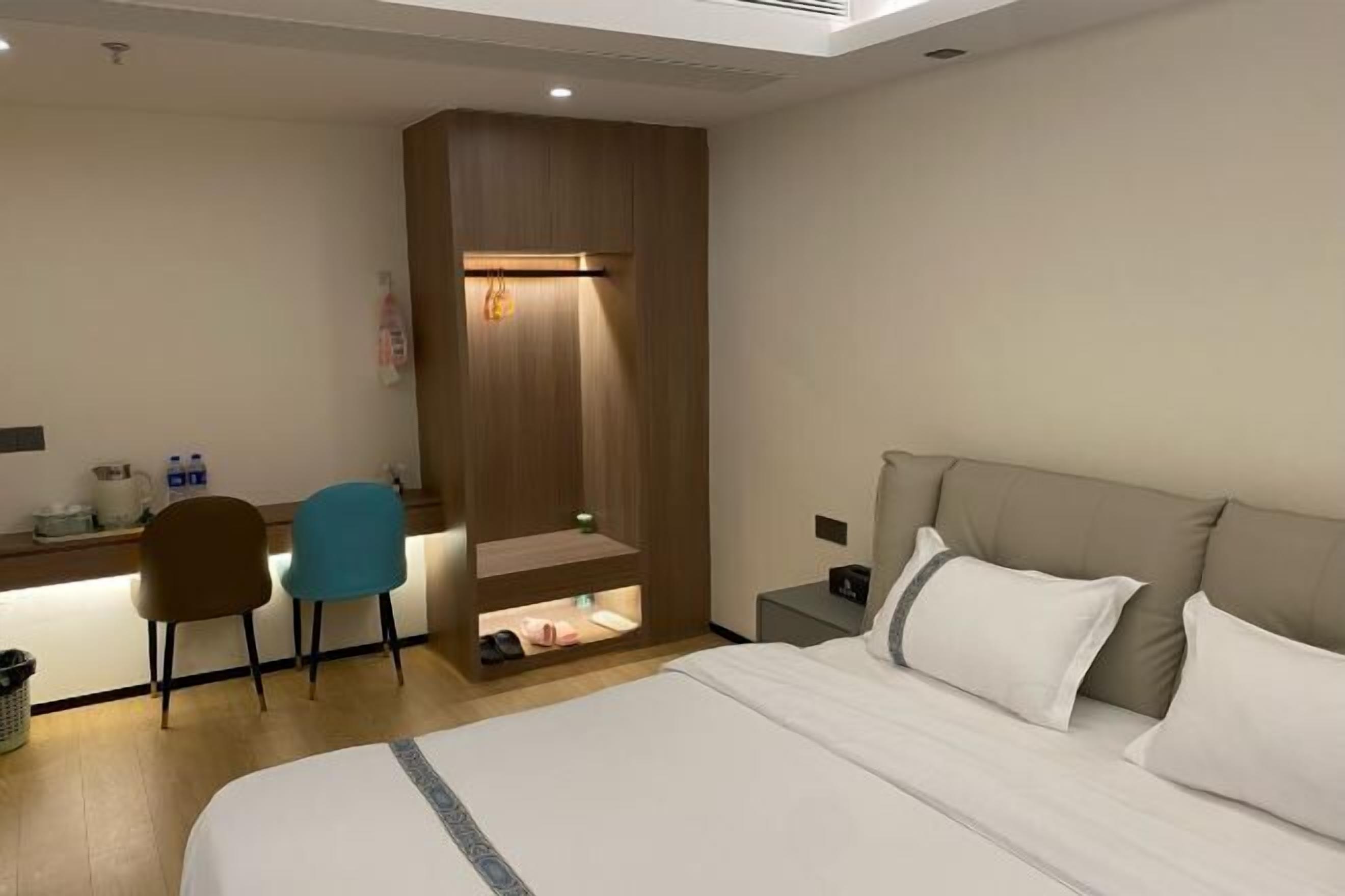 Una habitación de hotel con cama, escritorio, dos sillas, un mueble bajo y una mesita de noche.