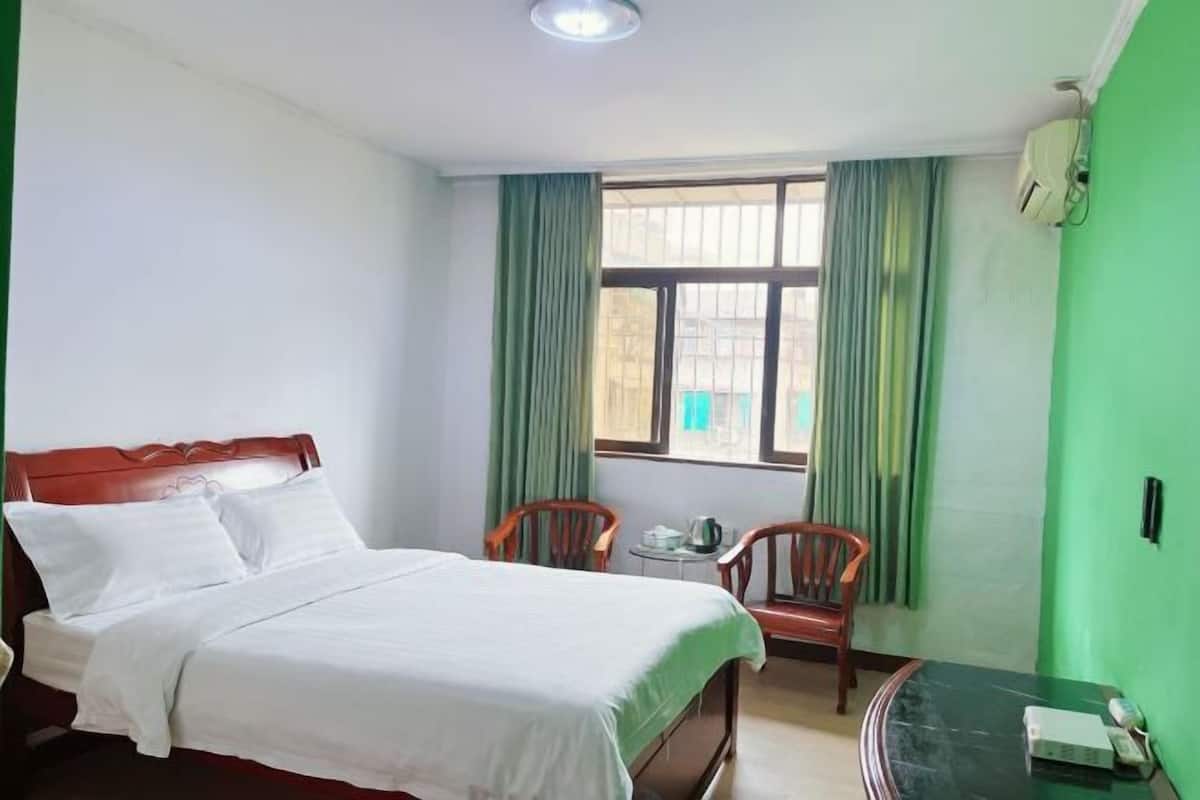 Una habitación de hotel con cama, dos sillas, una mesita y ventana con cortinas.