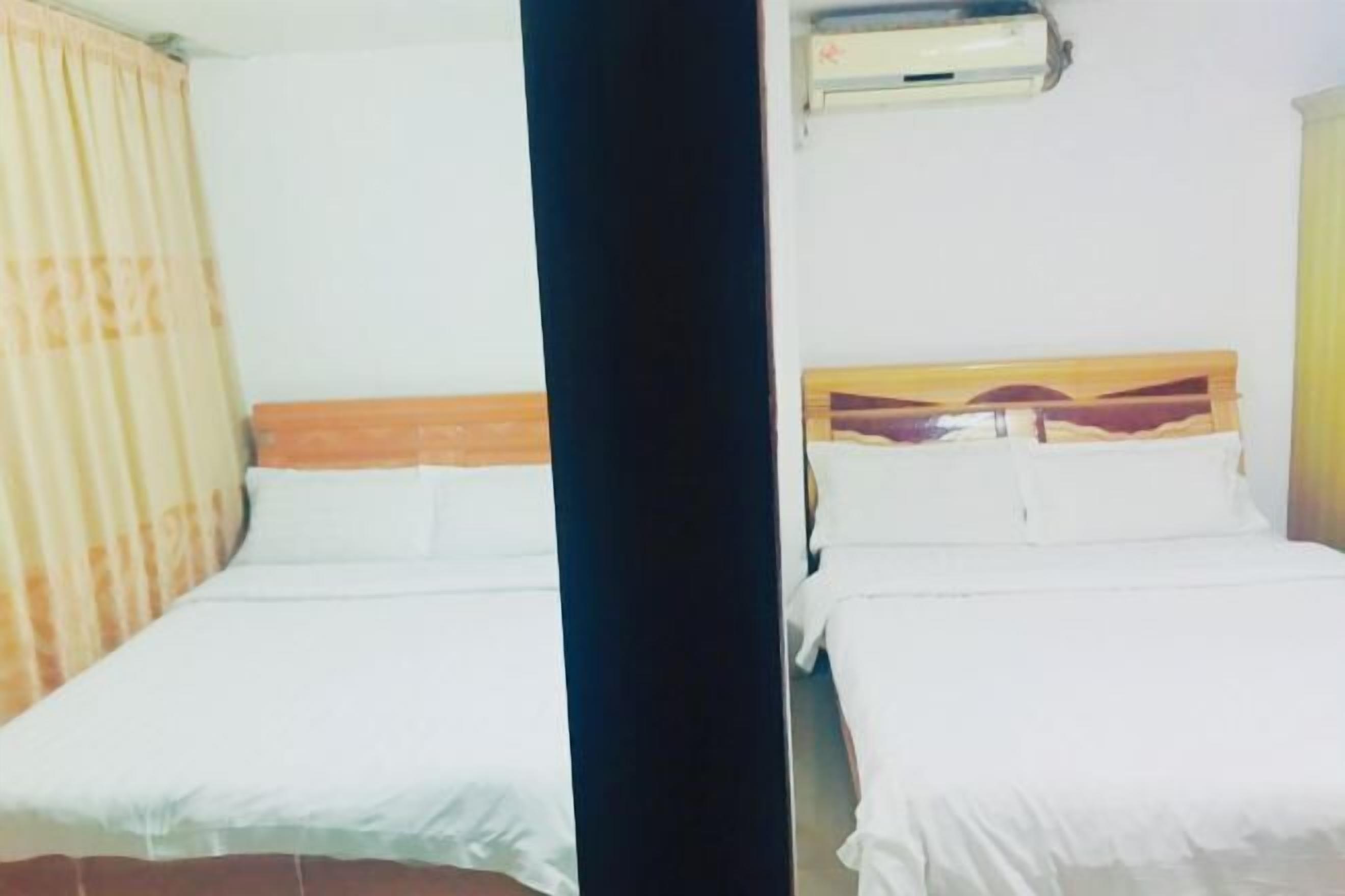 Una habitació amb dos llits, un capçal de fusta, roba de llit blanca i un aparell d'aire condicionat a la paret.