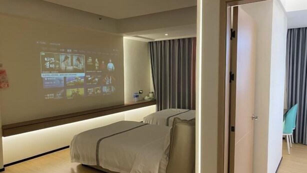 A hotel room with a bed, a bedside table, a wall-mounted projector, and a curtain. - Jixing Hostel (Shantou)