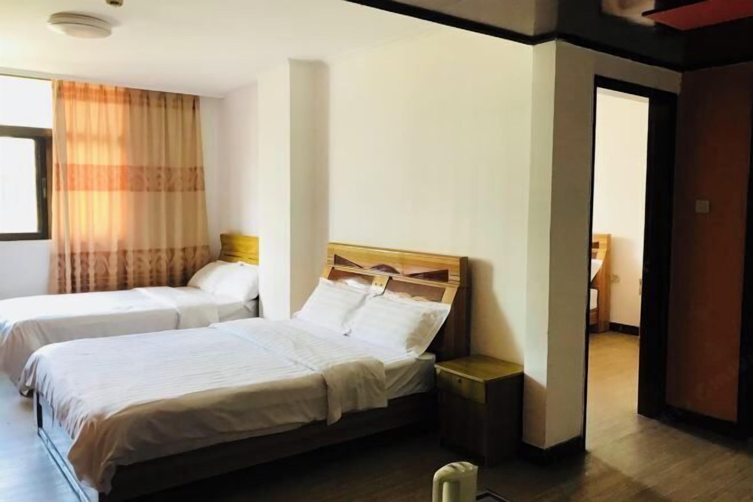Ein Hotelzimmer mit zwei Betten, einem hölzernen Kopfteil, einem Nachttisch und einem Fenster mit Vorhängen.