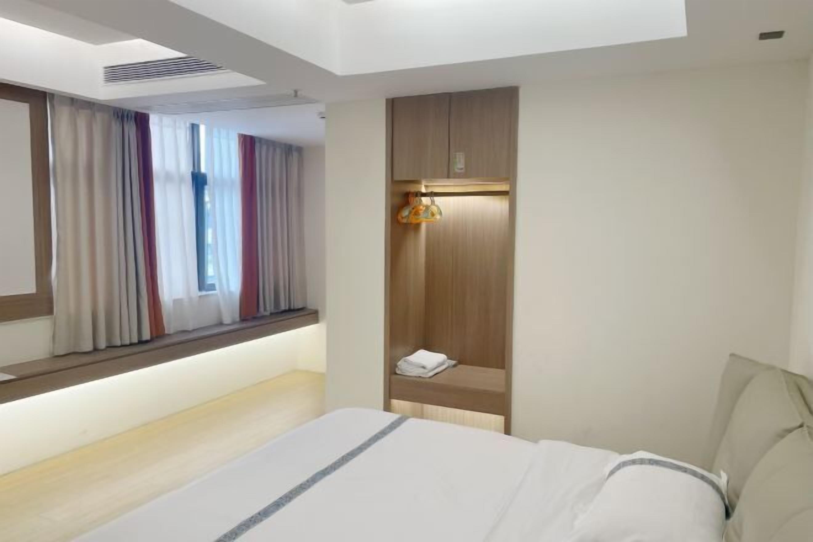 Habitación de hotel con cama, estante empotrado con toalla, ventana con cortinas y rejilla en el techo.
