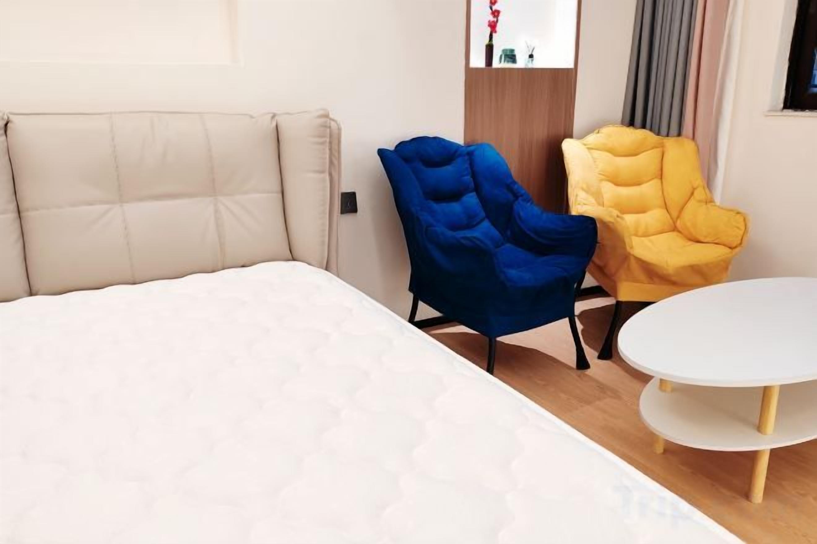 A bedroom with a bed, a blue chair, a yellow chair, and a small white table.
