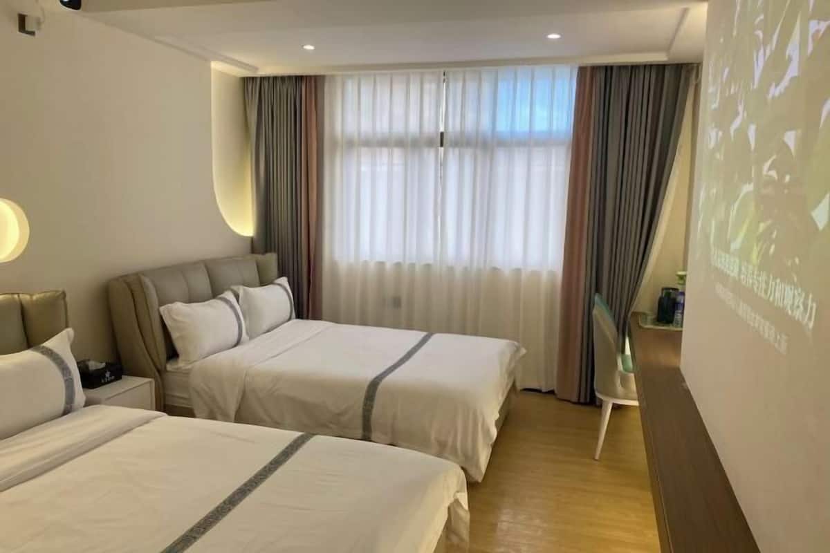 Habitación de hotel con dos camas, un ventanal con cortinas, una mesita y un proyector instalado en la pared.
