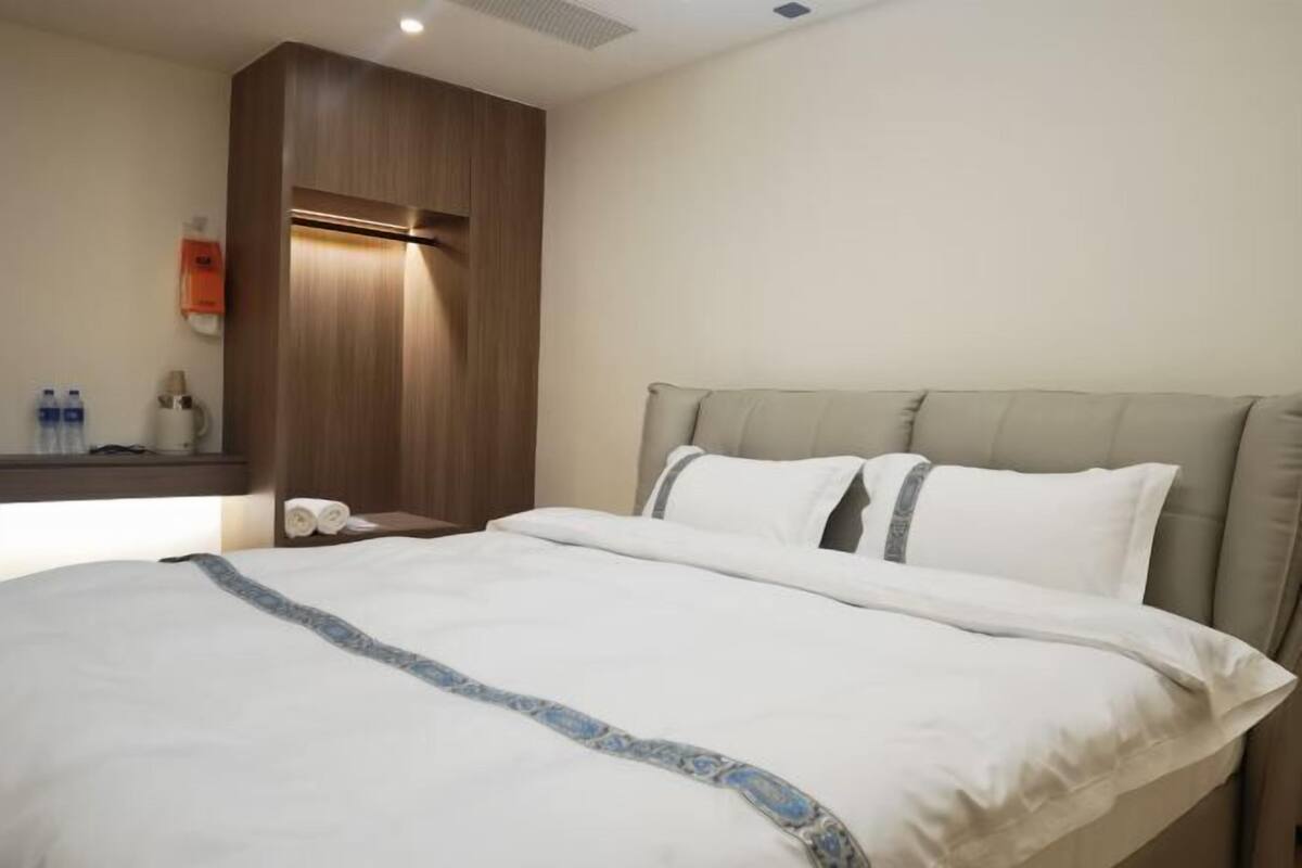 Habitación de hotel con cama, mesita de noche con artículos de aseo y pared de paneles de madera.