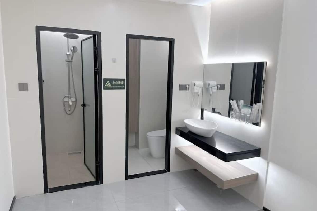 Un baño moderno con ducha, inodoro y tocador con lavamanos y espejo.