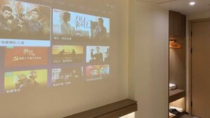 A projection screen displaying various scenes, a wooden shelf, and a door leading to a closet. - Jixing Hostel (Shantou)