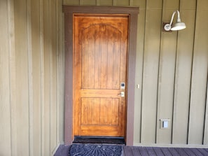Uma porta de madeira com puxador de metal e luminária acima.