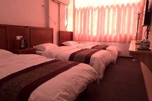 Ein Hotelzimmer mit drei Betten, einem Nachttisch mit Lampe und einem Fenster mit Vorhängen.