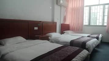A hotel room with three beds, a wooden headboard, a window with curtains, and a wall-mounted air conditioner.